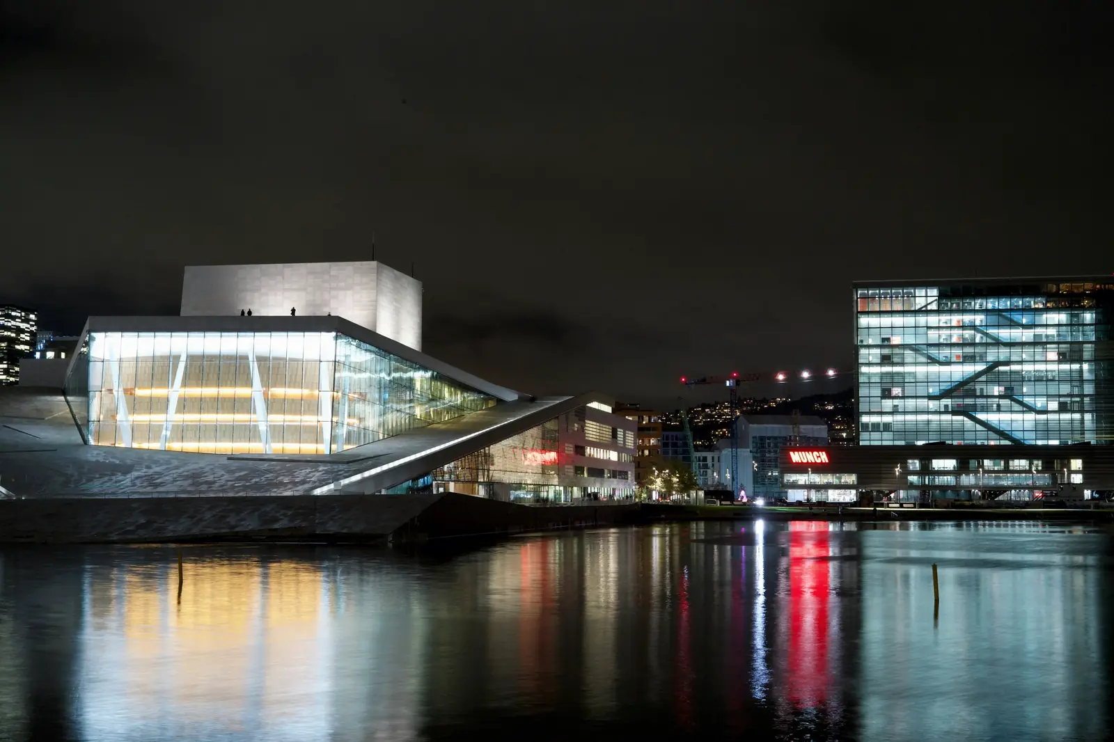 Moderne arkitektur i Oslo som speiler seg i vannet om kvelden